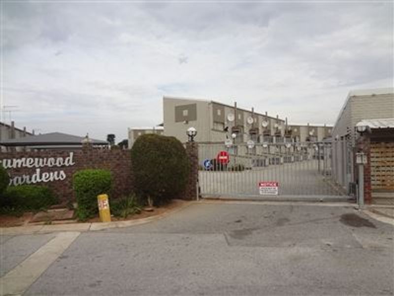 Front entrance view of the apartment complex featuring a secure gated access point and brick boundary wall.