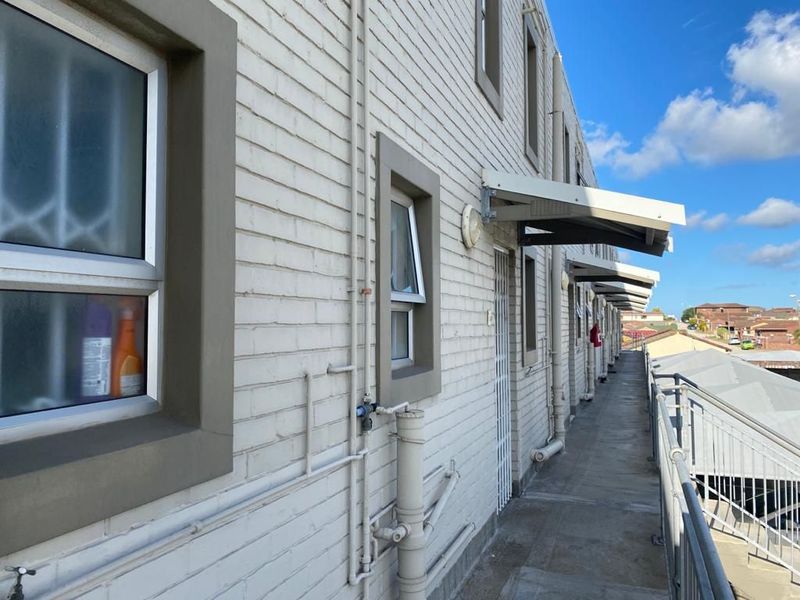 Exterior view of an apartment building walkway featuring painted brick walls, metal security gates, and protective awnings over the unit entrances.