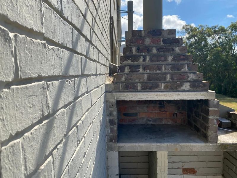 Outdoor patio area featuring a built-in brick braai structure against a painted brick wall, offering potential for an upgraded entertainment space.