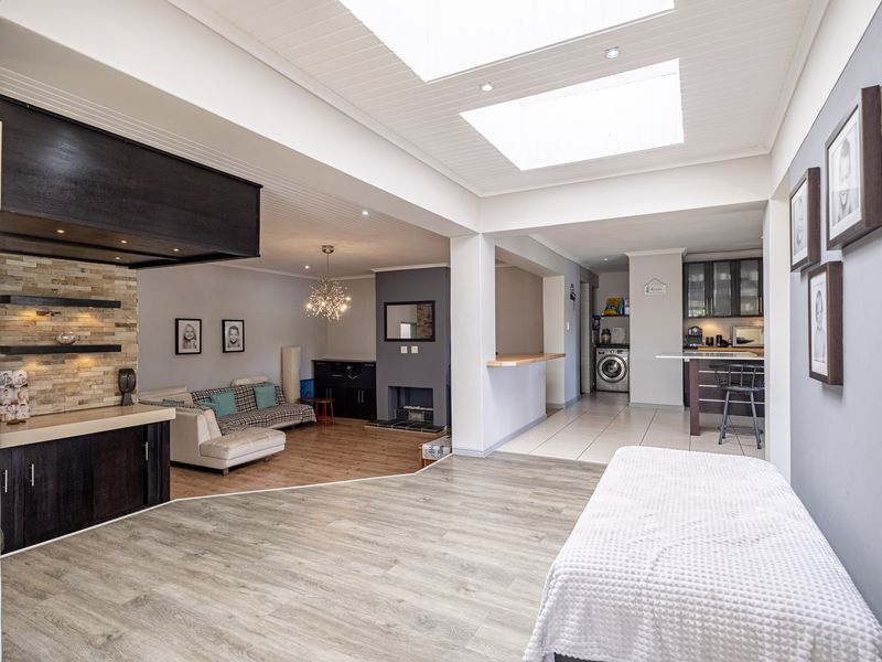 Spacious open-plan living area featuring modern laminate and tiled flooring, skylights, a stone feature wall, fireplace, and a functional kitchen with breakfast bar.