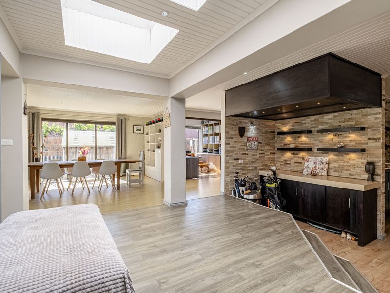 Spacious open-plan living area featuring a stone accent wall, built-in cabinetry, skylights, and seamless flow to the dining space and outdoor patio.