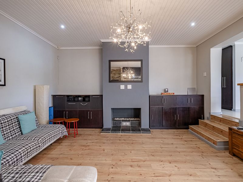 A well-maintained living room featuring timber flooring, a central fireplace with built-in cabinetry, and a distinctive tongue and groove ceiling with modern lighting.