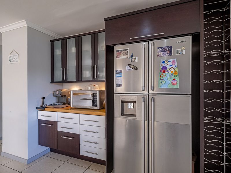 A functional kitchen area featuring two-tone cabinetry, a laminate countertop, and a dedicated integrated wine rack, finished with tiled flooring.