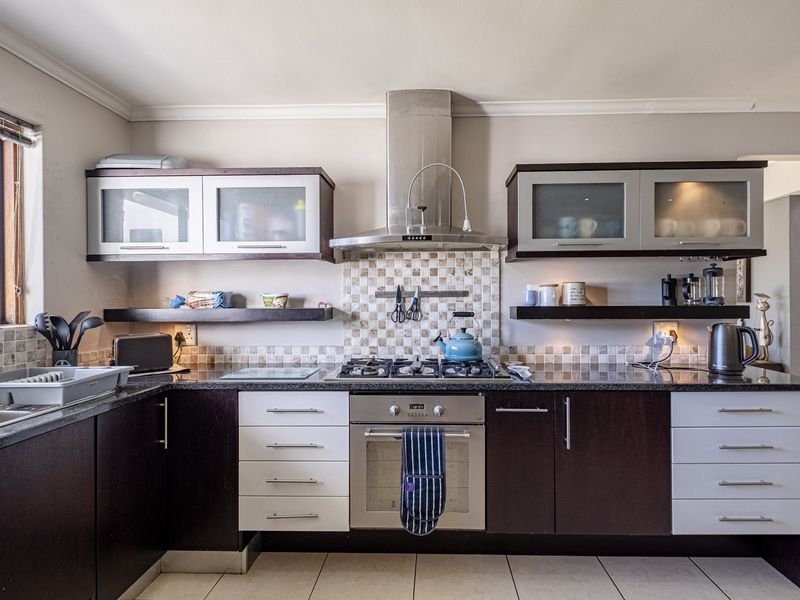 A functional kitchen featuring dark and light cabinetry, granite countertops, a gas hob, stainless steel extractor fan, and a tiled backsplash.