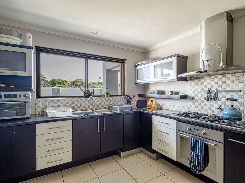 A functional kitchen featuring dark and light cabinetry, granite countertops, a gas hob, stainless steel oven, extractor fan, and a tiled backsplash.