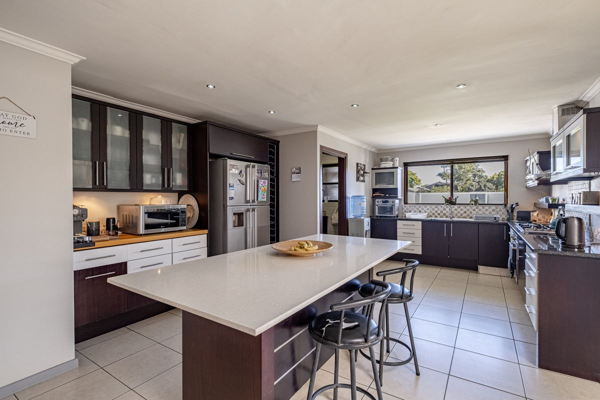 Spacious modern kitchen featuring a large central island with quartz countertops, dark wood cabinetry, tiled flooring, and integrated appliances.