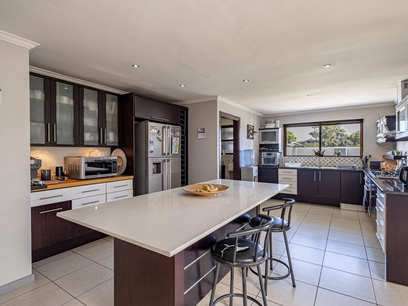 Spacious modern kitchen featuring a large central island with quartz countertops, dark wood cabinetry, tiled flooring, and integrated appliances.