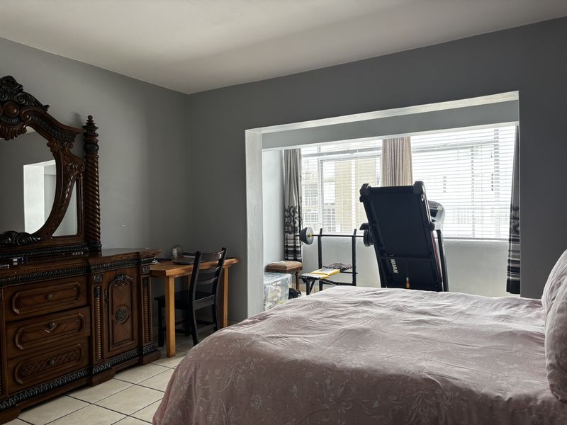 Spacious bedroom featuring tiled flooring and a recessed window area with venetian blinds, offering a versatile layout for sleeping and exercise.
