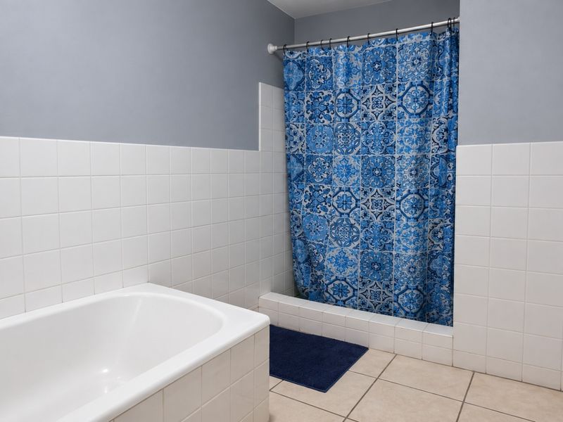 A functional bathroom featuring a built-in bathtub and a tiled shower enclosure with neutral wall and floor tiling.
