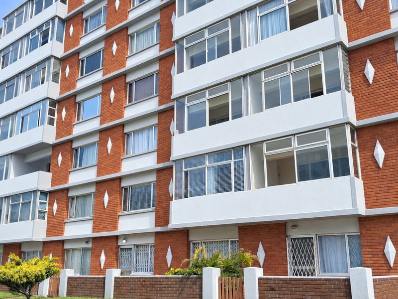 A multi-story apartment building featuring a red brick facade, white structural accents, and aluminium-framed windows with integrated security gates.