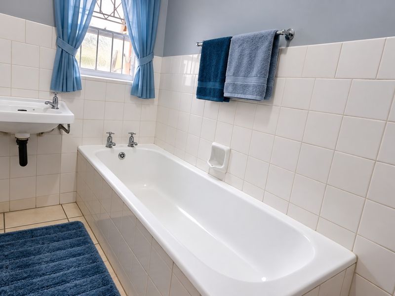 A functional bathroom featuring a built-in bathtub, wall-mounted basin, and neutral ceramic tiling throughout, offering a clean and practical space.