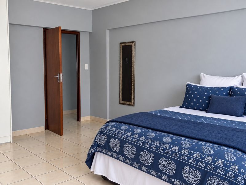 A well-maintained bedroom featuring neutral grey walls, light ceramic floor tiles, and a large built-in wardrobe with white finish.