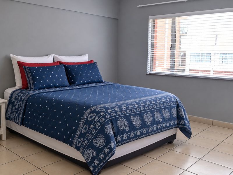 A simple bedroom featuring neutral grey walls, tiled flooring, and a window fitted with venetian blinds.