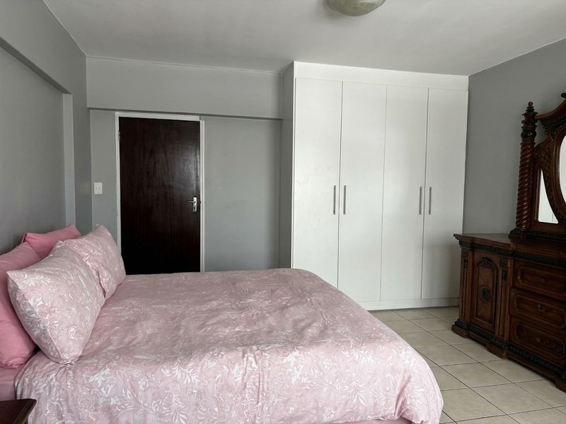 A well-maintained bedroom featuring neutral grey walls, tiled flooring, and ample built-in cupboard storage.