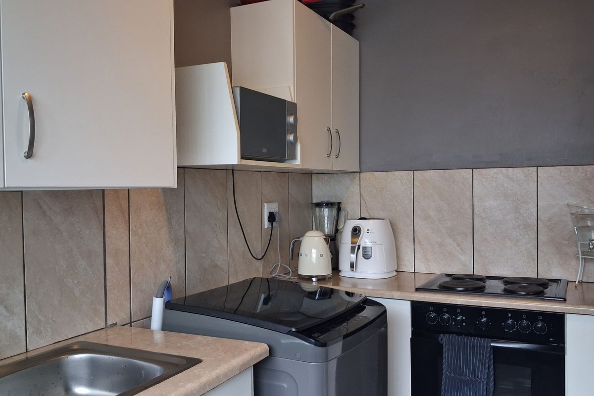A functional kitchen featuring white cabinetry, laminate countertops, a tiled backsplash, and integrated cooking appliances including an oven and electric hob.