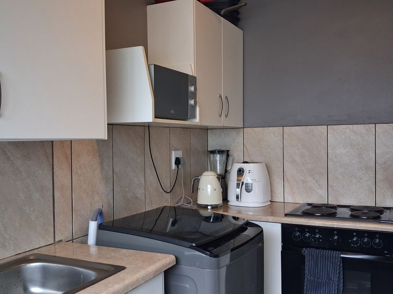 A functional kitchen featuring white cabinetry, laminate countertops, a tiled backsplash, and integrated cooking appliances including an oven and electric hob.