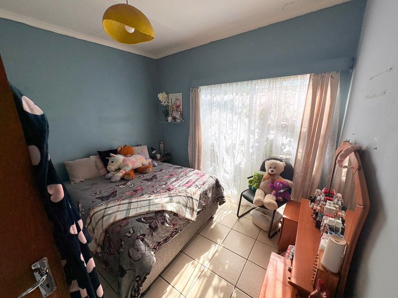 A bedroom featuring tiled flooring, a large window allowing natural light, and a central ceiling light fixture.