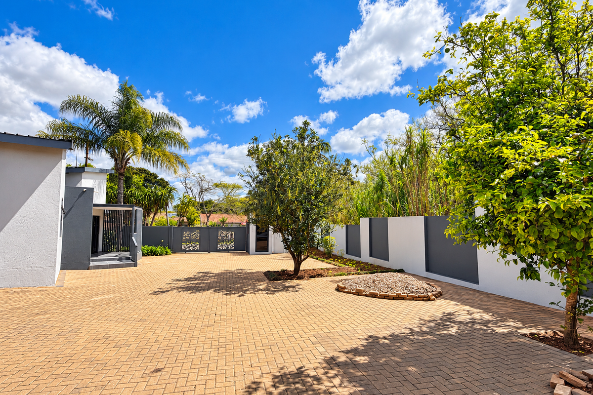 A well-maintained rear exterior area featuring extensive paving, modern boundary walls, decorative metal gates, and established garden landscaping.