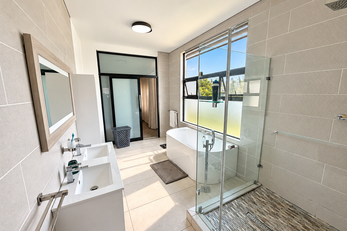 Modern bathroom featuring a double vanity, a sleek freestanding bathtub, and a spacious walk-in shower with a glass enclosure and decorative stone floor tiling.
