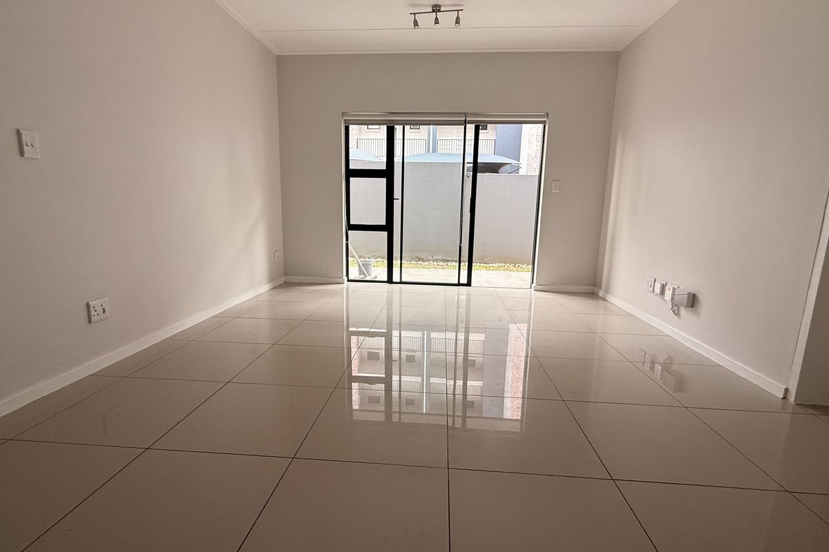 A bright, empty living room featuring polished porcelain floor tiles and a large sliding glass door providing access to the exterior.