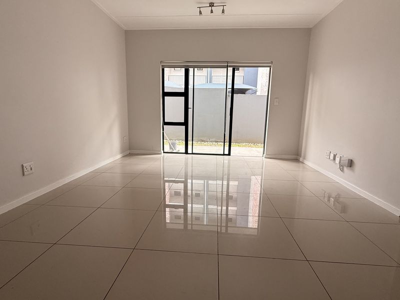 A bright, empty living room featuring polished porcelain floor tiles and a large sliding glass door providing access to the exterior.
