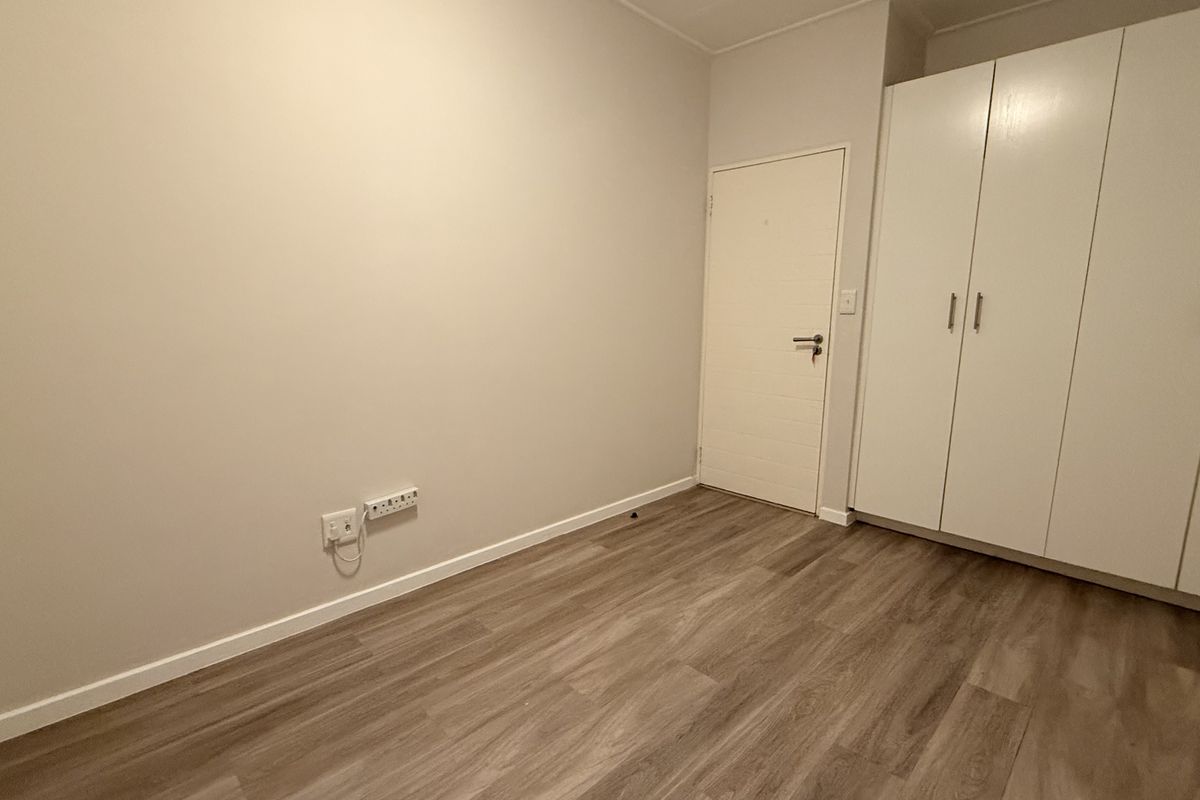 A clean, empty bedroom featuring modern laminate flooring and ample built-in cupboard storage space.