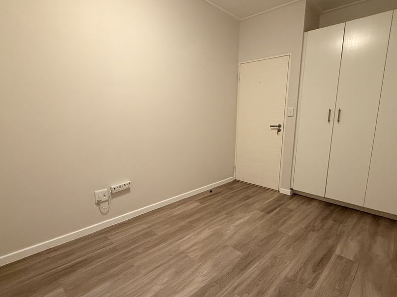A clean, empty bedroom featuring modern laminate flooring and ample built-in cupboard storage space.
