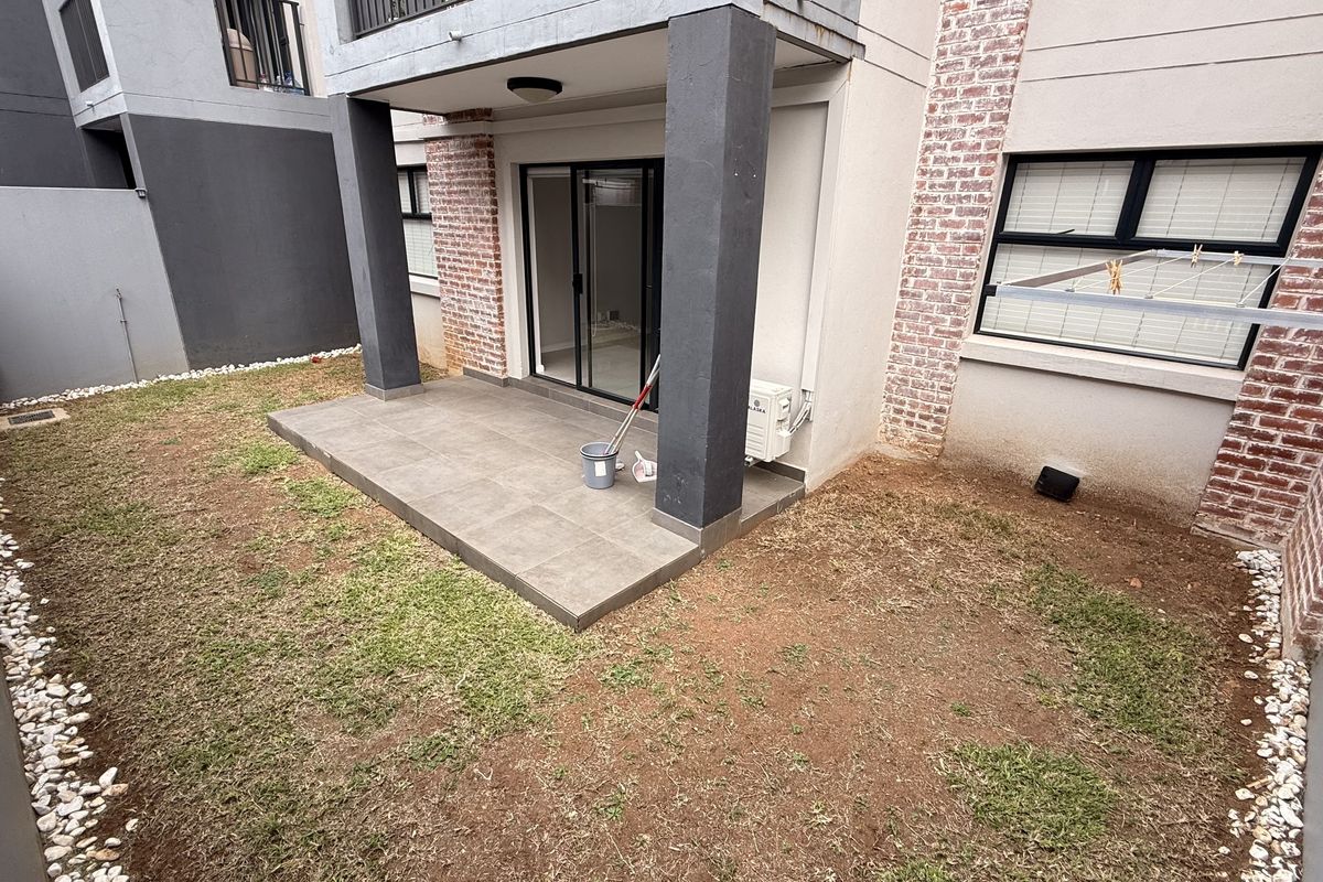 Rear view of the apartment featuring a covered tiled patio, exposed brick exterior walls, and a private garden area with a wall-mounted clothesline.