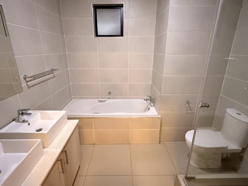 A modern, well-maintained bathroom featuring a double vanity, built-in bathtub, and a separate toilet area with a glass shower screen.
