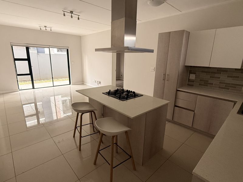 Modern open-plan kitchen and living area featuring a central island with gas hob, sleek cabinetry, and large sliding doors leading to the outdoor space.