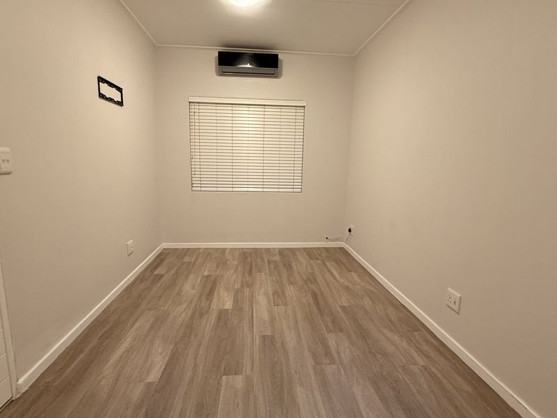 A clean, empty bedroom featuring modern laminate flooring, a wall-mounted air conditioning unit, and venetian blinds, providing a neutral canvas for personalization.