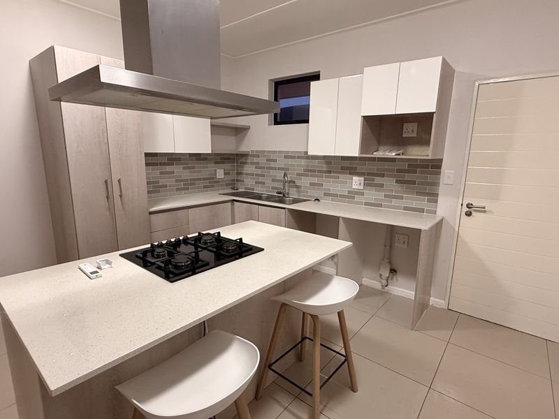 Modern kitchen featuring stone countertops, a central island with a gas hob, stainless steel extractor fan, tiled backsplash, and ample built-in cabinetry.