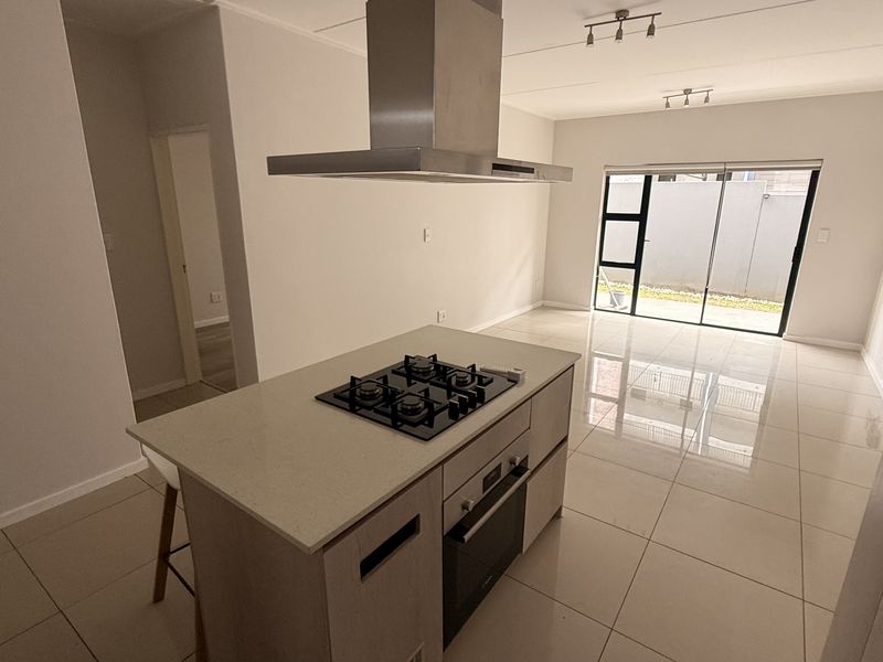 Modern open-plan living area featuring a sleek kitchen island with gas hob, built-in oven, extractor fan, and large sliding doors leading to the exterior.