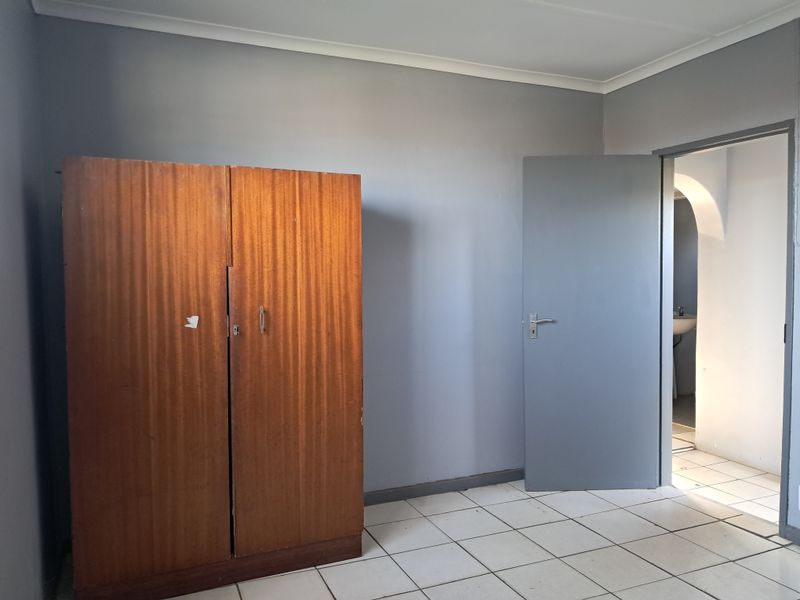 A simple bedroom featuring tiled flooring and neutral grey walls, with an adjacent doorway leading to a bathroom area.