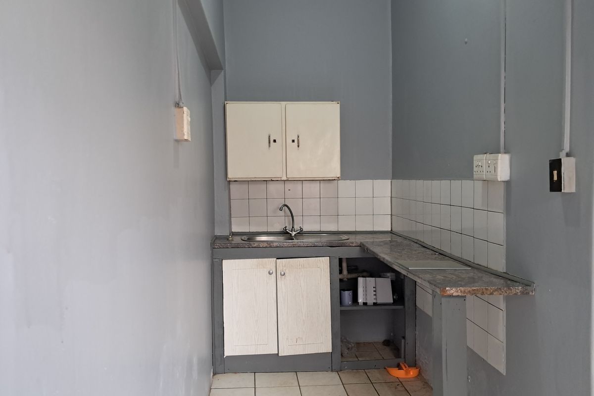 A compact, functional kitchen area featuring a stainless steel sink, tiled backsplash, and built-in cabinetry, offering potential for modernization and renovation.