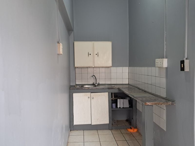 A compact, functional kitchen area featuring a stainless steel sink, tiled backsplash, and built-in cabinetry, offering potential for modernization and renovation.
