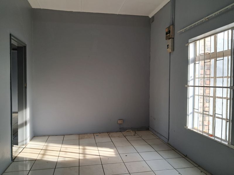 An empty bedroom featuring tiled flooring, a window with security bars, and an exposed electrical distribution board on the wall.