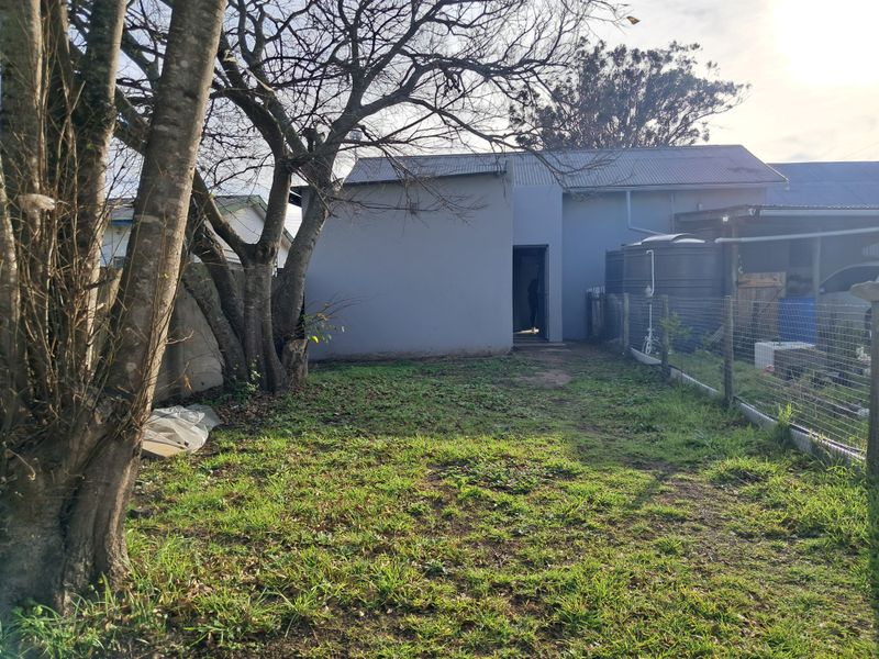 Rear view of the property featuring a lawn area, wire fencing, and a water tank adjacent to the building structure.