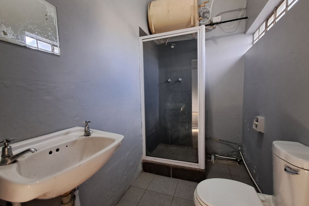 A dated bathroom featuring a shower enclosure, pedestal basin, and toilet, with exposed plumbing and visible wear on wall finishes.