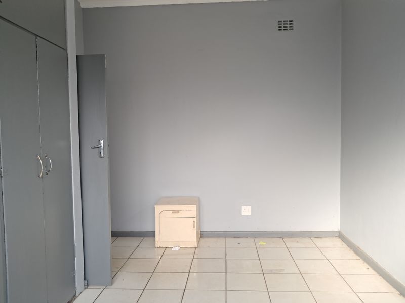 A vacant bedroom featuring built-in cupboards, tiled flooring, and neutral grey walls, offering a blank canvas for personalization.