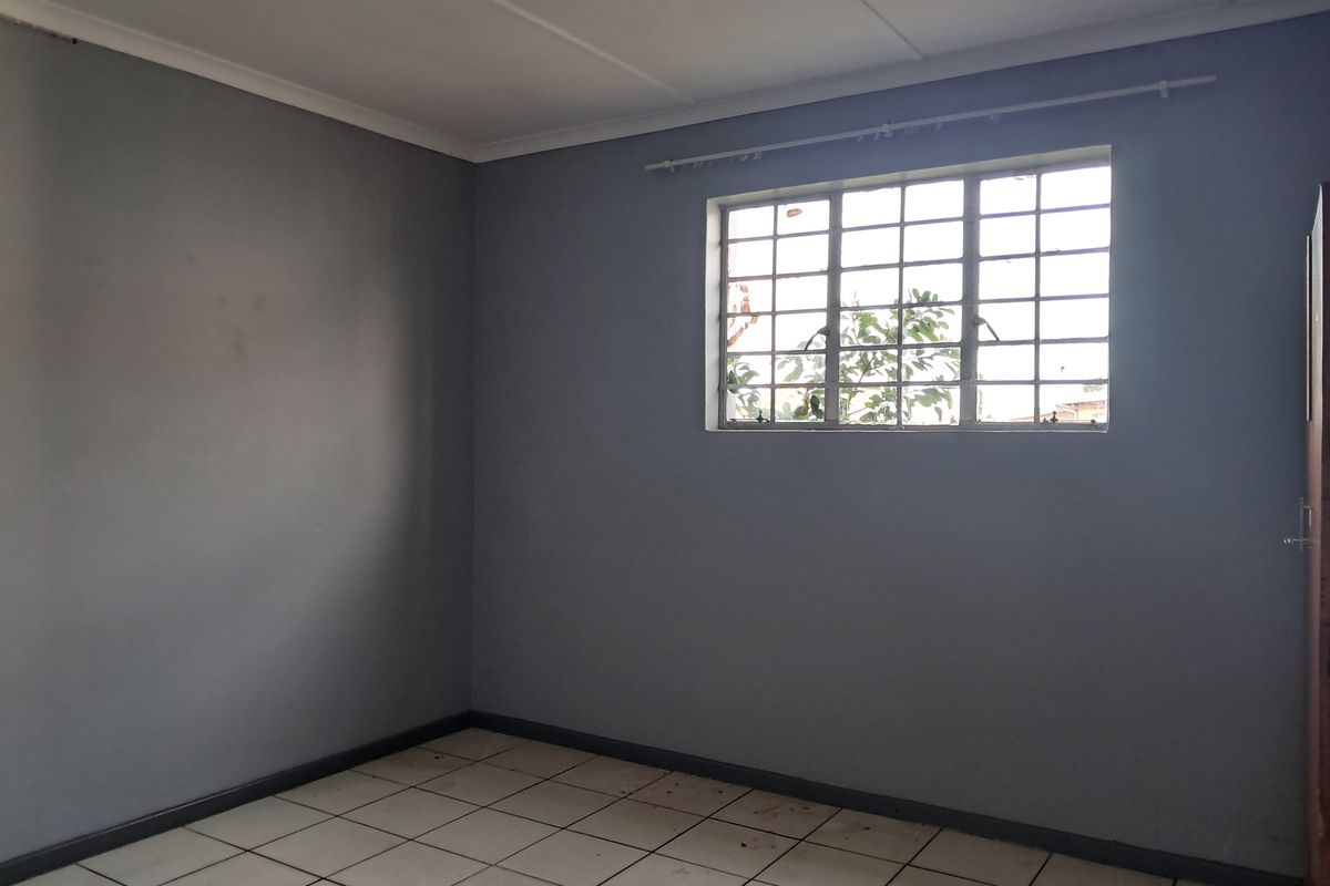 An empty bedroom featuring grey painted walls, tiled flooring, and a window fitted with security burglar bars.