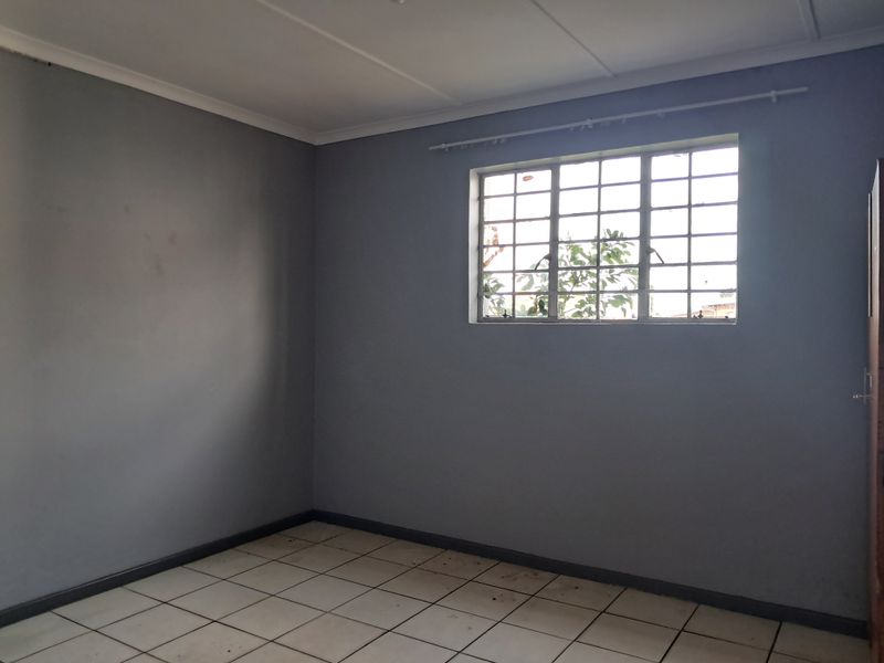 An empty bedroom featuring grey painted walls, tiled flooring, and a window fitted with security burglar bars.