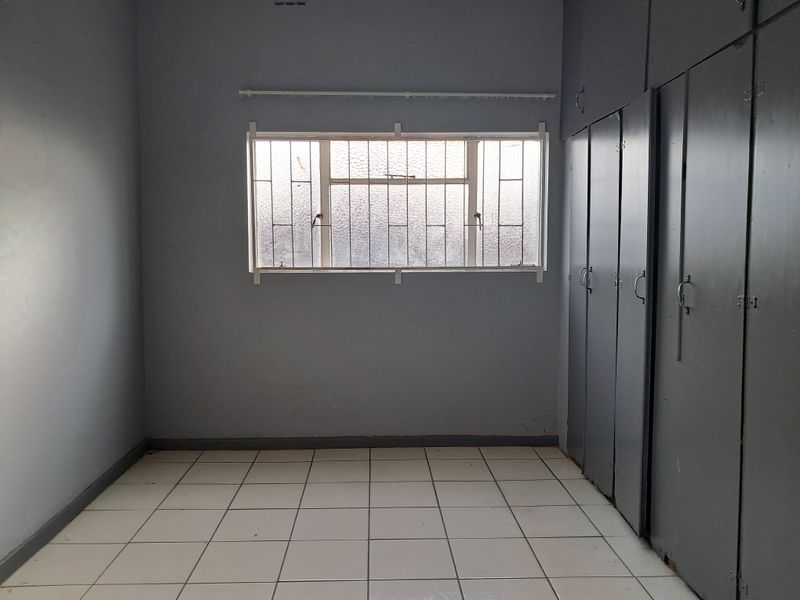 An empty bedroom featuring tiled flooring, built-in cupboards, and a window fitted with security bars.