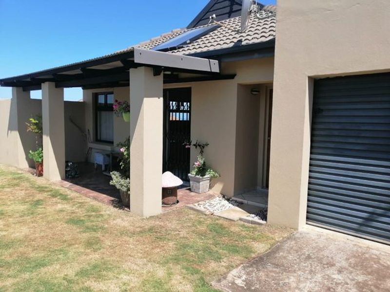 Front view of the house featuring a covered patio, secure entrance, garage, and solar water heating system installed on the tiled roof.