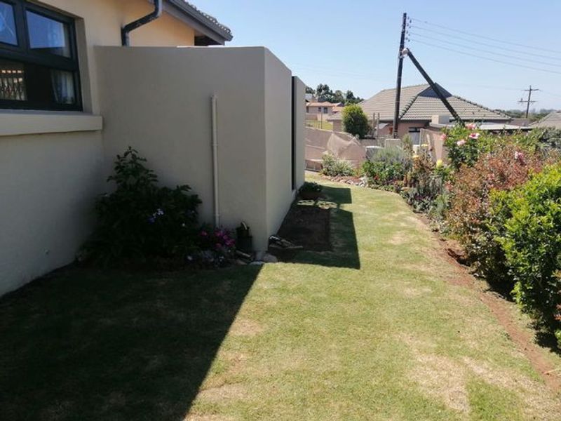 A side garden area featuring a well-maintained lawn, established garden beds, and a clean exterior wall with a functional downpipe.
