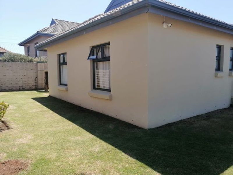 Rear view of the property featuring plastered exterior walls, aluminium window frames, a tiled roof, and a security camera installed on the corner.