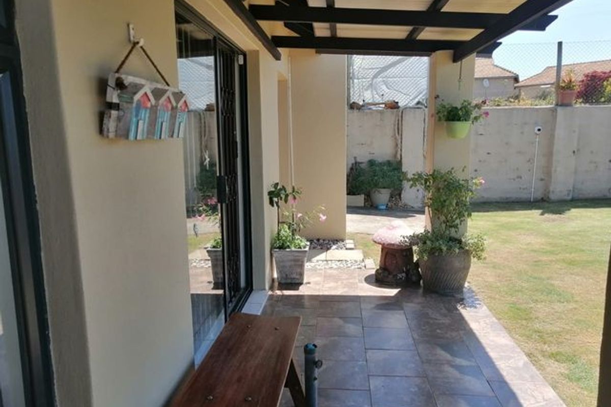 A covered patio area featuring tiled flooring and direct access to the garden through a sliding glass door.