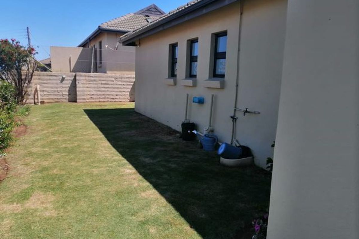 A view of the rear exterior of the house featuring a lawn, concrete boundary wall, and external wall-mounted water taps.