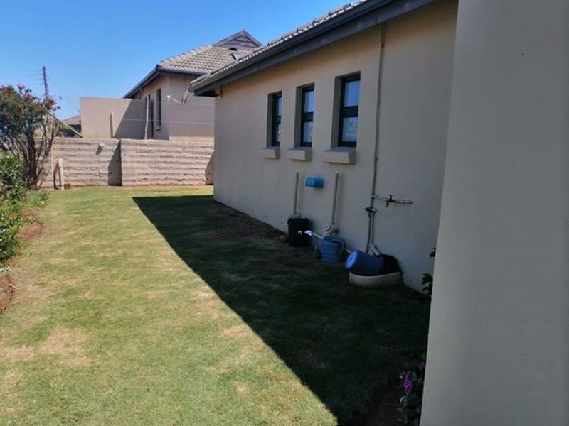 A view of the rear exterior of the house featuring a lawn, concrete boundary wall, and external wall-mounted water taps.