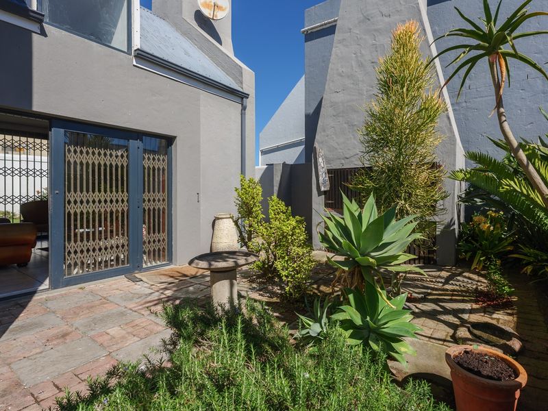 A private rear courtyard featuring a paved patio area, built-in braai, and direct access to the interior living space through sliding glass doors.